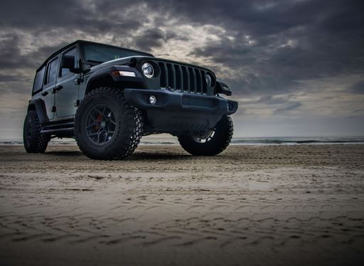 A dark Jeep Wrangler on the beach on a cloudy day