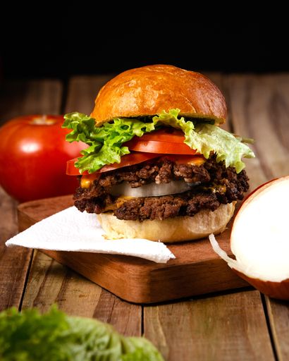 A vertical shot of a delicious hamburger on a wooden plate with a black background