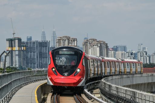 The view of a red Mass Rapid Transit on the railroad before the cityscape under the cloudy sky