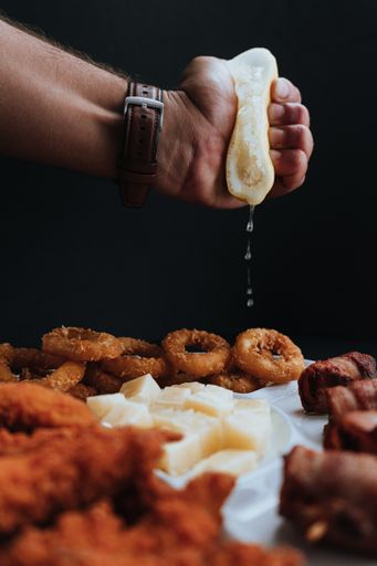 A vertical shot of a man squeezing lemon on fried onion rings and other food