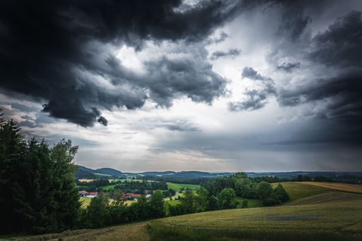 The dramatic thunderclouds over a field with green trees