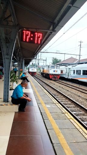 A vertical shot of people in masks waiting for the afternoon train to arrive in Jakarta, Indonesia