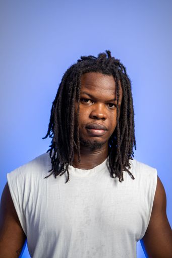 A closeup vertical shot of a black person with a serious stare against a blue background