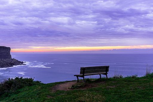 An idyllic view of a sea from the cliff with a bench under a cloudy sky - perfect for wallpaper