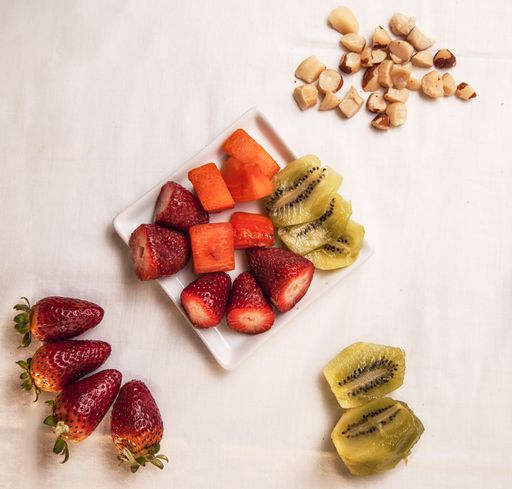 A high angle shot of strawberries, kiwi, carrots, and almond on a white surface