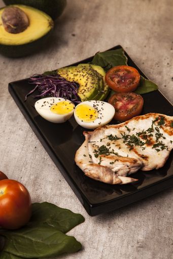 A vertical closeup shot of grilled chicken with eggs, tomatoes, avocado and cabbage