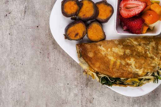 A high angle closeup shot of a vegetarian omelet with greens and a bowl of fruits and sweet carrots on the side