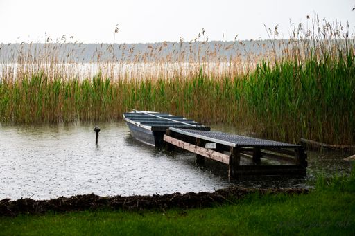 An empty boat near a dock in the marsh during rain.