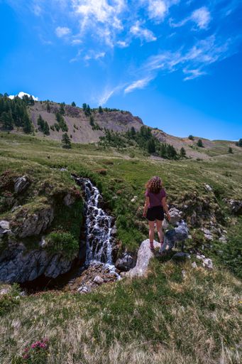 A vertical of a female with her dog standing against a river flowing through park of Milfons Lakes