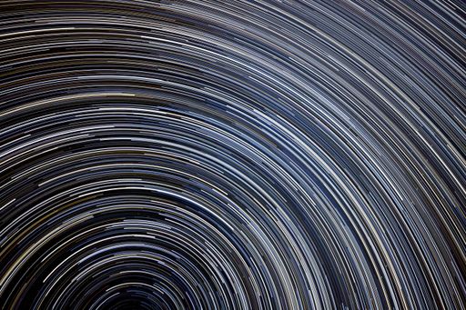A star trails in the night sky with sweeping curves of white and blue against a dark background