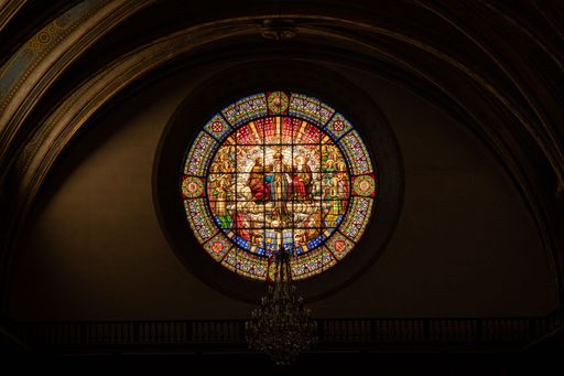 An interior view of an old church with a stained glass window of religious paintings
