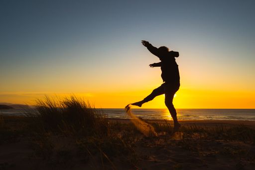A silhouette of a man jumping and enjoying a sunset on the beach
