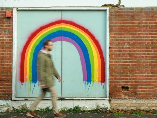 A blur shot of a male walking past a door with a rainbow painted on it