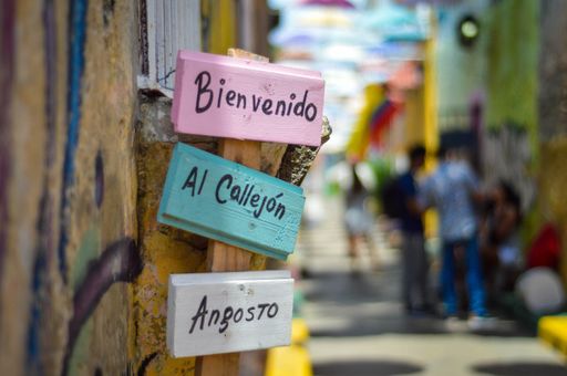 A selective focus shot of a sign in Spanish which says 'Bienvenido Al Callejon Angosto' - Translation: 'Welcome to the Narrow Alley'