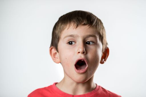 A portrait of an astonished Caucasian small boy with an open mouth against the white background