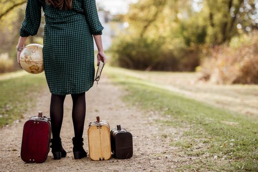 A closeup shot of a female standing on a pathway near her old suitcases while holding the bible and a desk globe