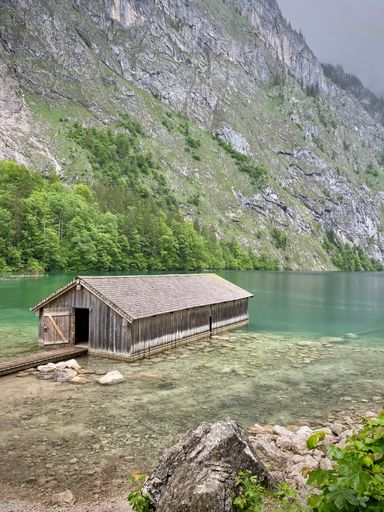 A wooden boat house at the shore of Lake Obersee in Bayern Germany with a green hill in the background