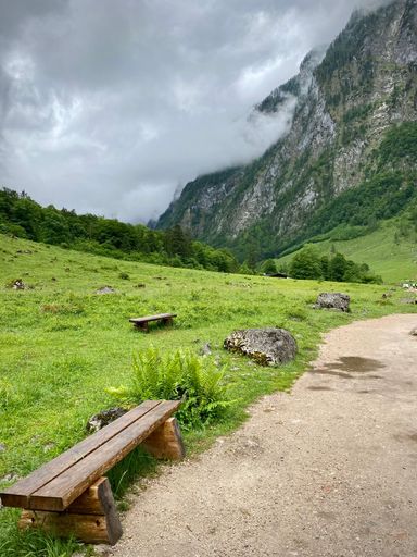 A vertical shot of wooden benches on the path to the mountains covered in clouds in Bayern Germany