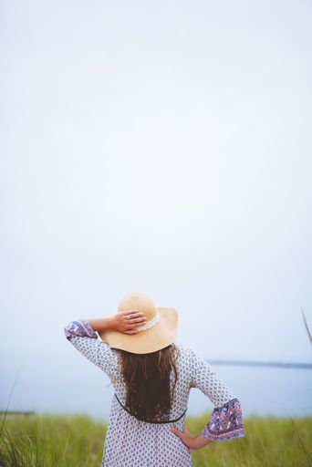 A female wearing a summer hat with her hand on her hip looking in the distance with a blurred background