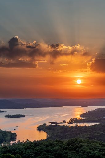 A vertical shot of the sunset over the lake and the sun shining through the clouds