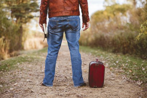 A male standing on an empty pathway near his old suitcase while hiding the bible