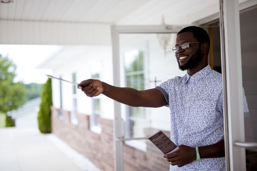 A shallow focus shot of a male standing near a door and giving out pamphlets  while smiling