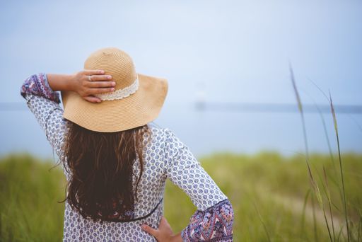 A beautiful shot from behind of a female wearing a summer hat with her hand on her hip and a blurred background