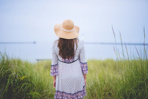 A beautiful shot from behind of a female wearing a summer hat and standing in a grassy field with a blurred background