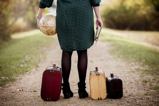 A female standing on an empty road near her suitcase while holding the bible and a globe