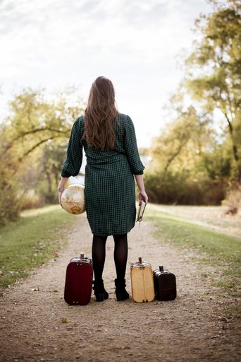 A vertical shot of a female standing on an empty near her old suitcase while holding the bible and a desk globe