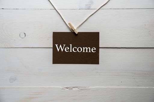 A closeup shot of a sign with welcome written on it and a white wooden background
