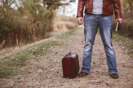 A male standing on an empty road near his old suitcase and holding the bible with a blurred background