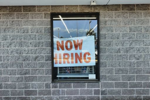 A now hiring sign seen through a window glass