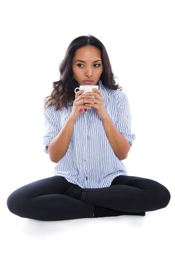A vertical shot of a young woman sitting cross-legged drinking a cup of tea against a white background