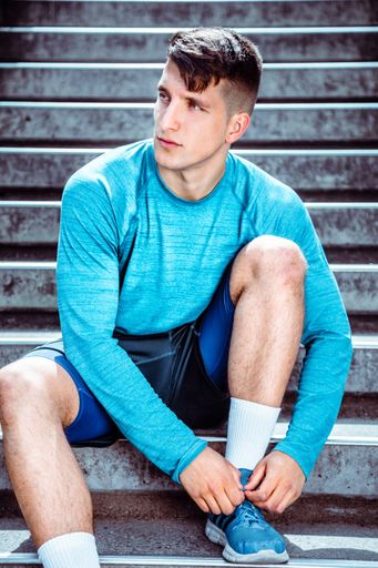 A vertical shot of an athletic young man sitting on stairs tying his shoelaces to go for a run