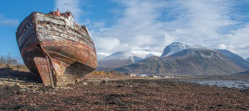 An old rusty ship on a dry shore with cloudy mountains in the background