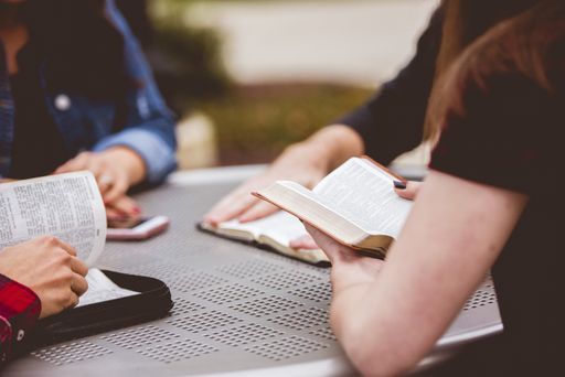 A closeup shot of females sitting around the table reading the bible with a blurred background