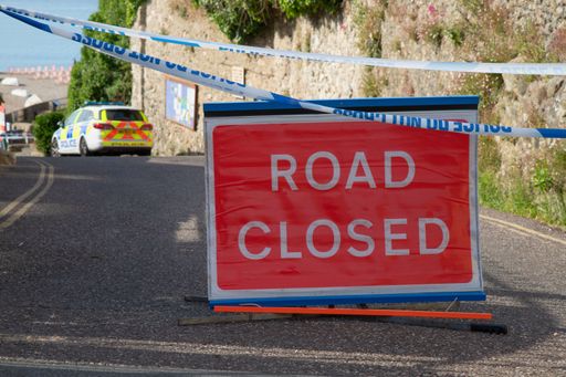 A display of a road sign indicating the closure of the road on the pavement next to barricade tapes