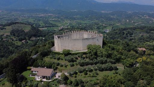 A bird's eye view of a medieval fortress on a green hill surrounded with trees