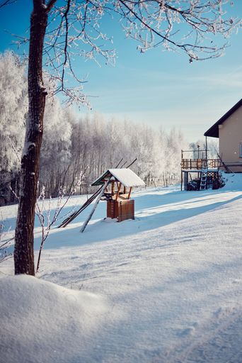 A vertical shot of a wooden well covered in snow in countryside during winter