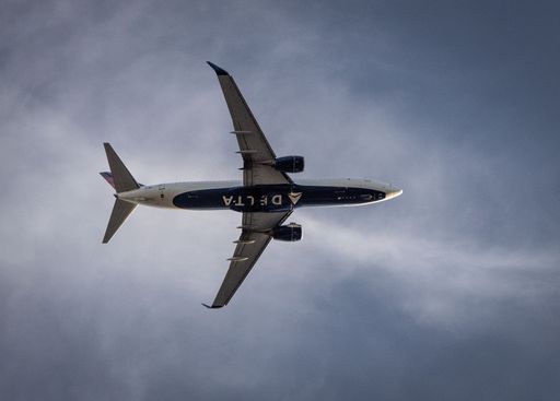 A low-angle view of a Delta plane flying against a blue cloudy sky