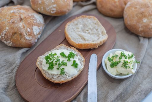 A closeup shot of Crusty round bread rolls topped with parley and cream on a wooden board