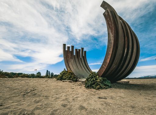 An old corten steel arc sculpture on the beach in Vancouver, Canada, in blue sky background