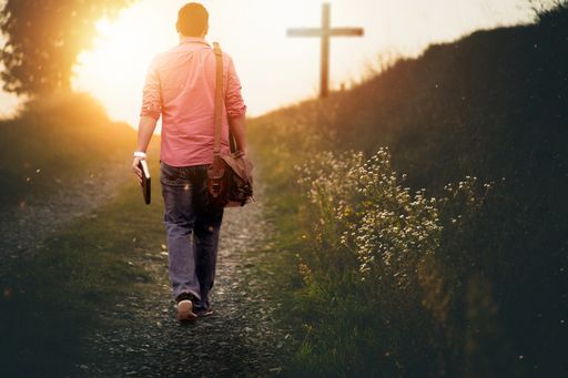 A male holding the bible walking up to the hill towards the cross with a blurred background