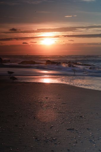 A vertical shot of sea waves covering the beach in the sunset