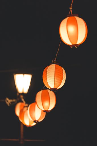 A vertical shot of orange paper lanterns hanging from a wire spreading light during nighttime