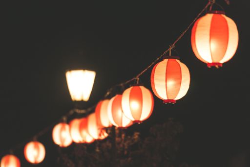 A selective focus shot of orange paper lanterns hanging from a wire and spreading light during nighttime