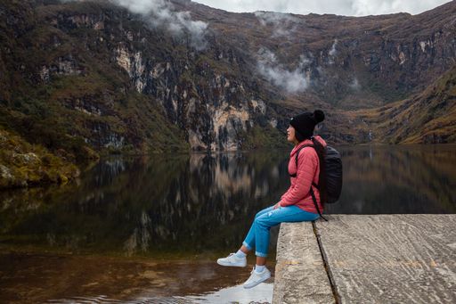 A girl in a pink jacket with a backpack sitting by the lake and looking at nature in the mountains