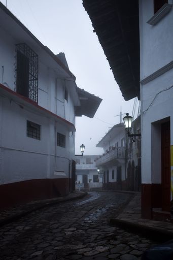 A narrow street surrounded by residential buildings on a rainy and foggy day