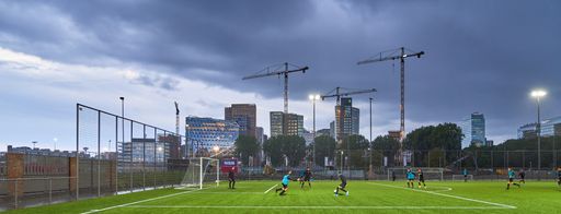 A panoramic shot of people playing football with buildings in the distance under a cloudy sky